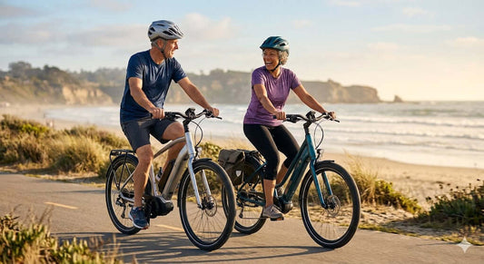 An active couple over 50 riding silver and teal step-through electric bikes on a paved coastal path, highlighting easy-mounting low-step frames for seniors